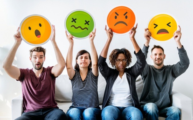 Gruppe von Menschen hält farbige Emoticons hoch, die verschiedene Gefühlszustände darstellen.