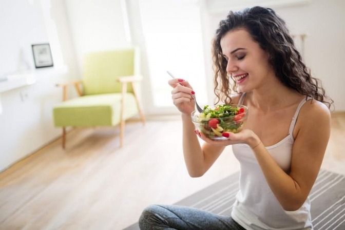 Eine junge Frau isst einen bunten Salat mit Lebensmitteln, die alle einen hohen Vitamin C Gehalt aufweisen.