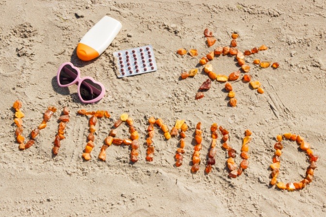 Sonnencreme und Sonnenbrille neben Schriftzug Vitamin D am Strand
