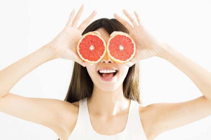Eine Frau hält eine Grapefruit mit vielen Vitaminen vor ihr Gesicht