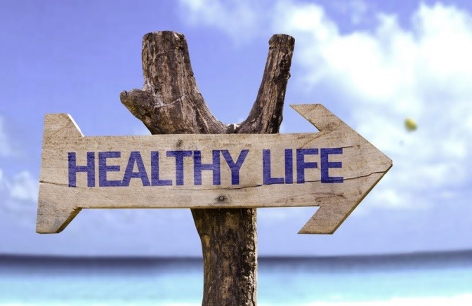 Ein Holzschild in Pfeilform an einem Strand, welches nach rechts zeigt und die Aufschrift "Healthy Life" trägt.