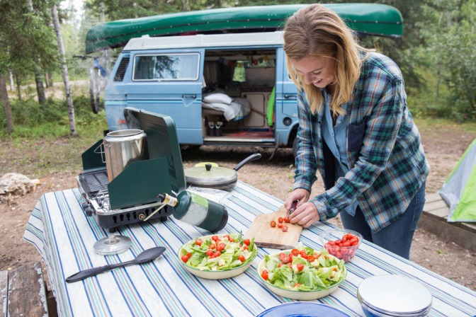 Frau bereitet ein Abendessen auf einem Campingplatz zu.