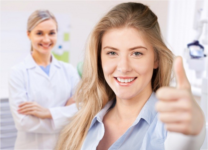 Eine Frau zeigt einen Daumen hoch, eine Ärztin ist im Hintergrund