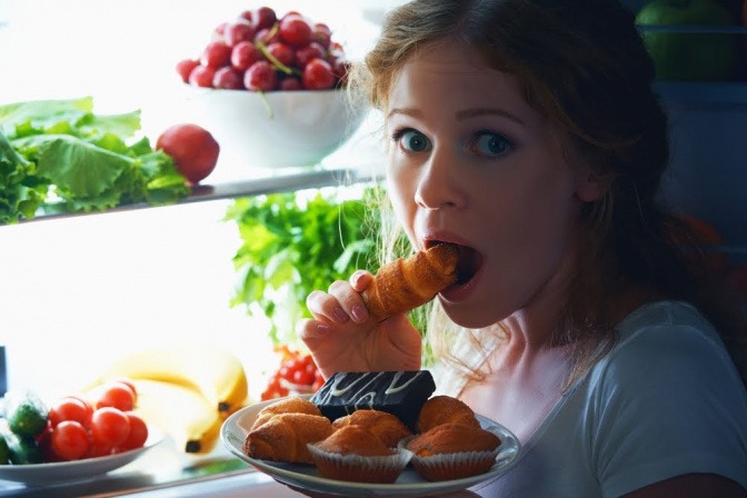 Die Frau, die in diesem Bild vor dem Kühlschrank kniet und ungesunde Snacks isst, hat die Antwort auf die Frage "was soll ich kochen?" für sich selbst bereits beantwortet. Doch gesund essen geht auch mit wenig Zeitaufwand. 