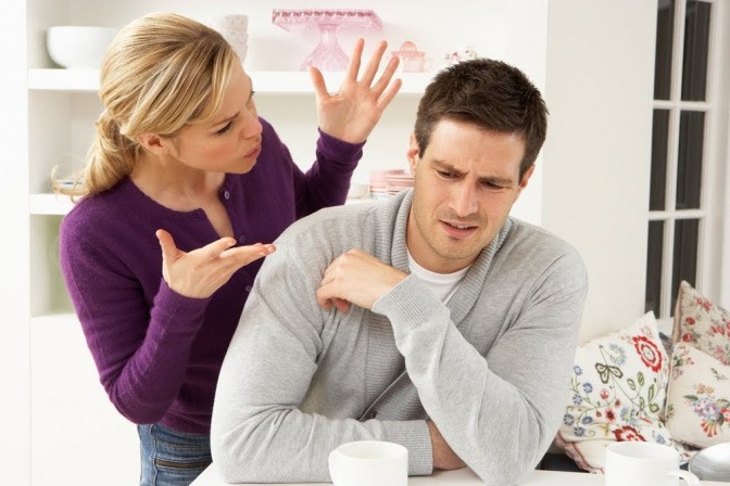 Ein Paar streitet sich, vielleicht über die Frage "Was tun gegen Eifersucht?". Sie gestikuliert wild mit den Händen, während er resigniert am Tisch sitzt. 