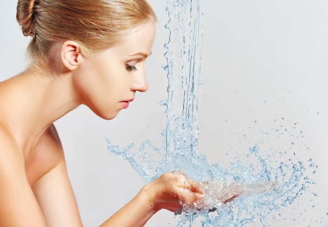 Eine Frau will sich das Gesicht mit Wasser waschen