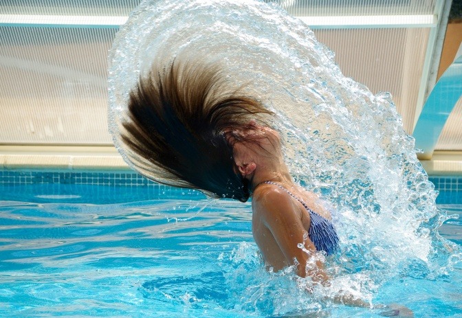 Frau im Swimmingpool taucht aus dem Wasser auf und wirft lange Haare nach hinten