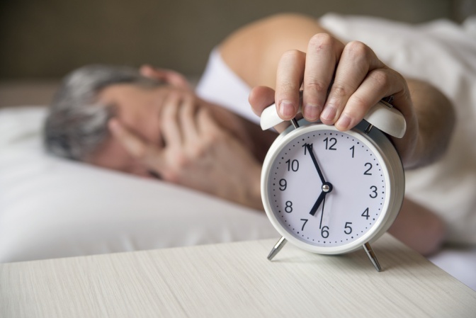 Mann im Bett greift auf Wecker