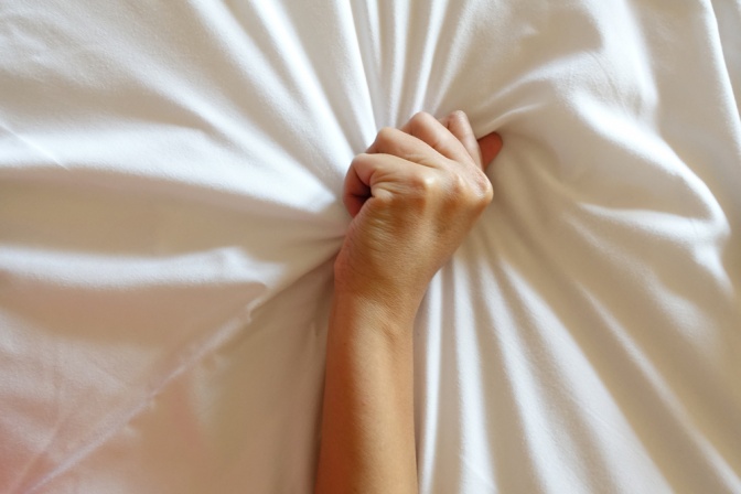 Eine Hand hält verkrampft wegen einem weiblichen Orgasmus ein Leintuch