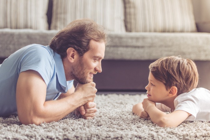 Vater und Sohn liegen auf einem Teppich und schauen sich glücklich an
