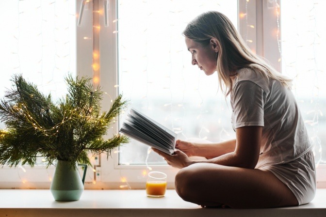 Frau sitzt mit Kerzen am Fensterbrett und liest
