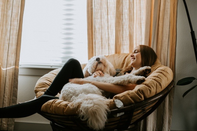 Frau kuschelt mit ihrem Labradoodle in einem großen Sessel.