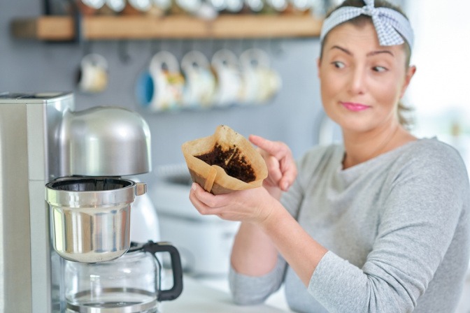 Frau nimmt eine benutzte Filtertüte aus einer Kaffeemaschine, um sie zur Wespenabwehr zu nutzen.