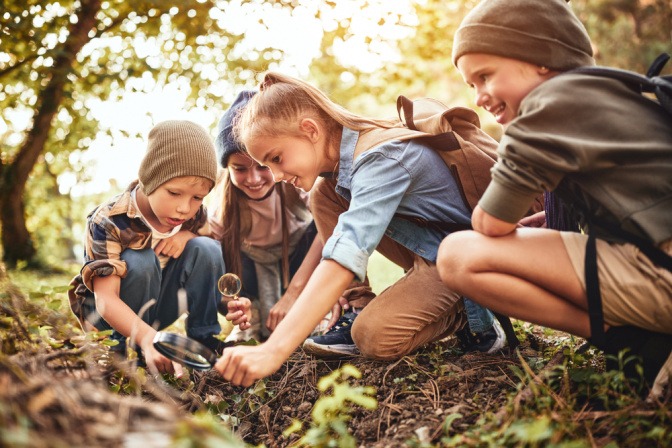 Kinder untersuchen mit einer Lupe den Boden im Wald