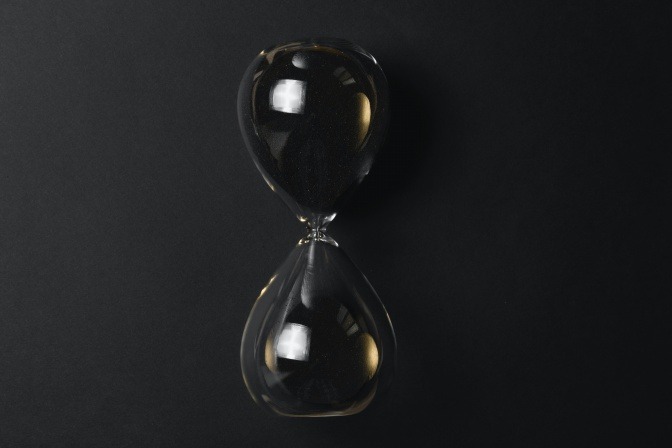 Eine Sanduhr aus Glas mit schwarzem Sand. 