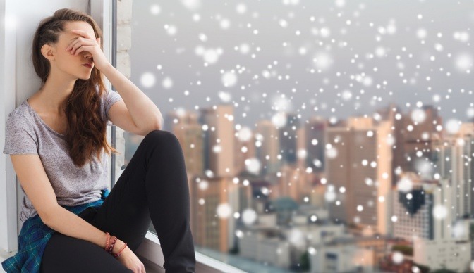 Junge Frau sitzt im Winter verstimmt am Fensterbrett