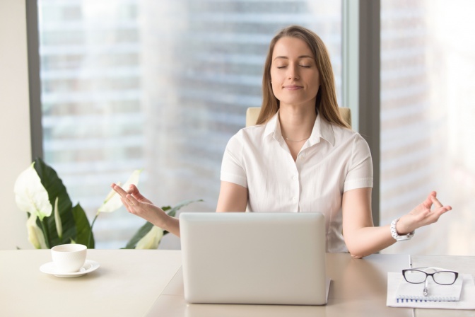 Frau sitzt vor ihrem Laptop ohne Stress und meditiert