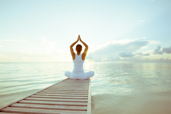 Eine Frau sitzt am Ende eines Stegs und entspannt mit Yoga