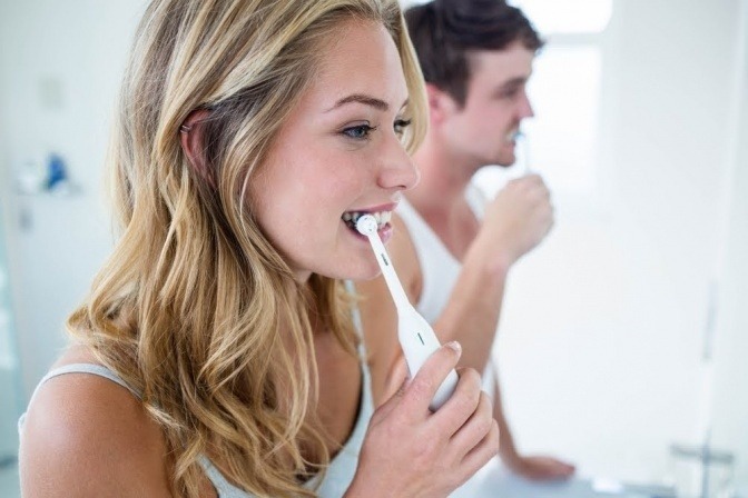 Mann und Frau bei der Zahnpflege von Implantaten mit elektrischer Zahnbuerste