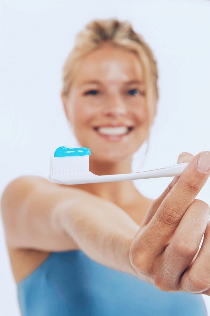 Eine Frau zeigt blaue Zahnpasta zur Zahnpflege bei Implantaten
