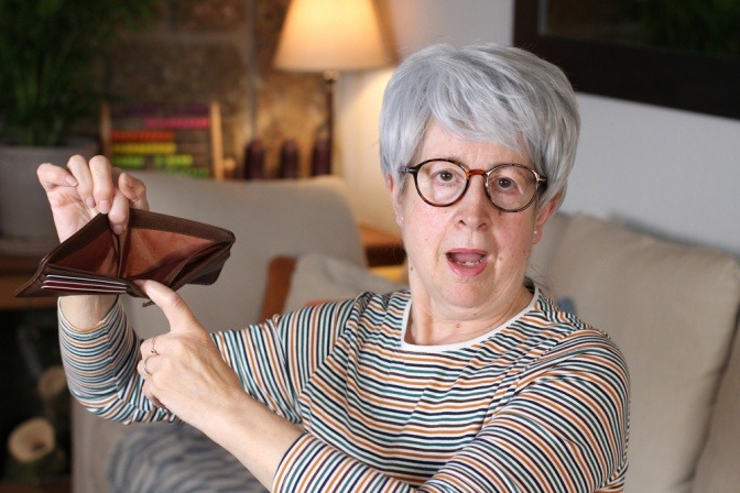 Eine Seniorin hält geschockt ihre leere Geldbörse in die Höhe.
