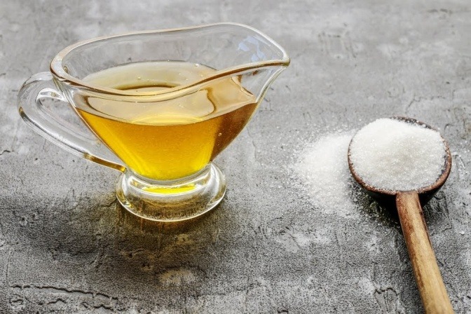 Eine kleine Karaffe mit Ahornsirup, daneben liegt ein Esslöffel mit Kristallzucker.
