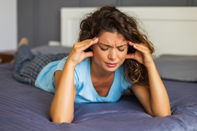 Beunruhigte und gestresste junge Frau liegt auf dem Bett und zerbricht sich den Kopf über ein Problem.