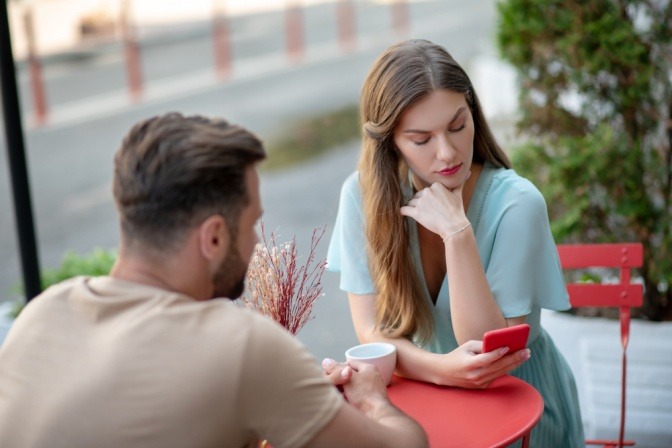 Paar im Cafe, sie blickt auf ihr Handy, er schaut teilnahmslos in der Gegend rum.