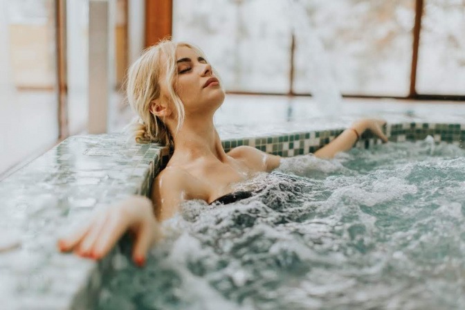 Eine Frau entspannt in einem Whirlpool, ihre Arme ruhen auf dem Beckenrand, ihre Augen sind geschlossen.