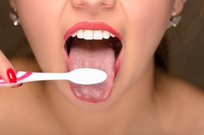 Eine Nahaufnahme einer jungen Frau, die sich die Zunge mit einer Zahnbürste putzt.