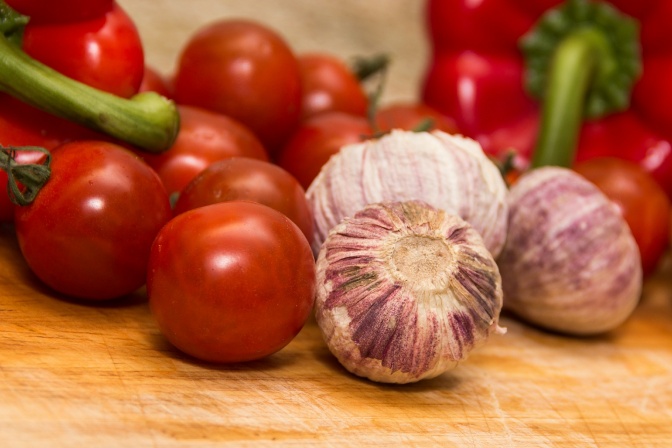 Viele Tomaten liegen neben drei Zehen Knoblauch