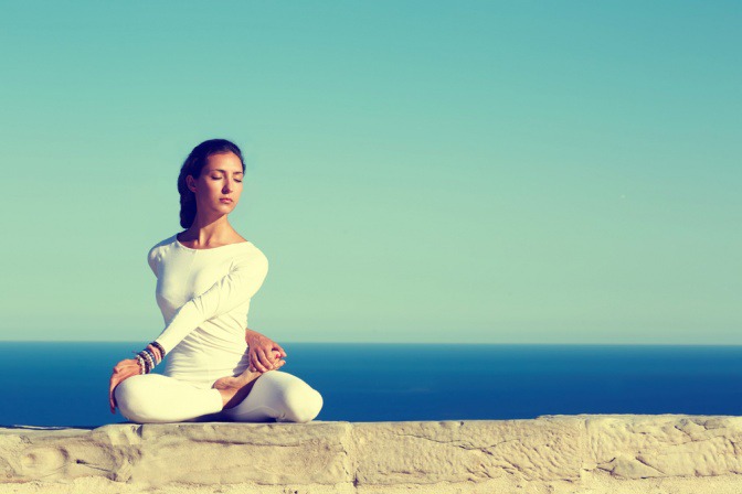 Auf dem Foto ist eine junge Frau zu sehen, die in der Natur Yoga macht. Sie befindet sich an einem See.