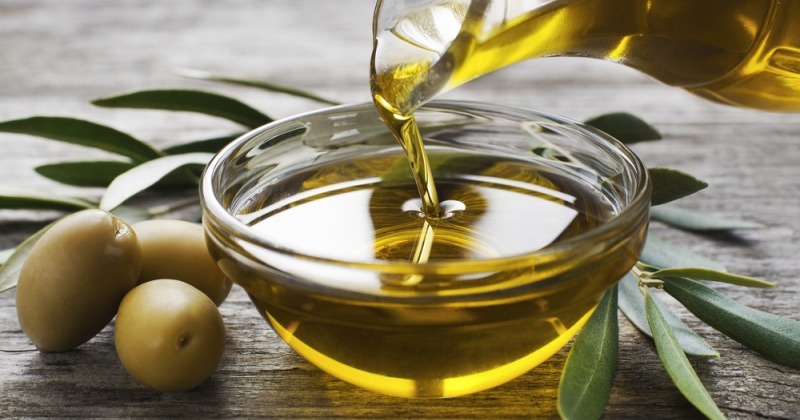 Olivenöl fließt aus einer Kanne in eine Schüssel