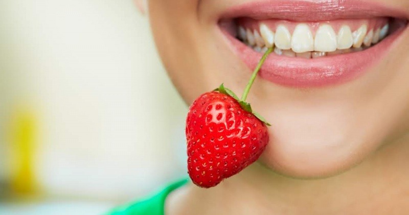 Eine Frau hat eine Erdbeere im Mund