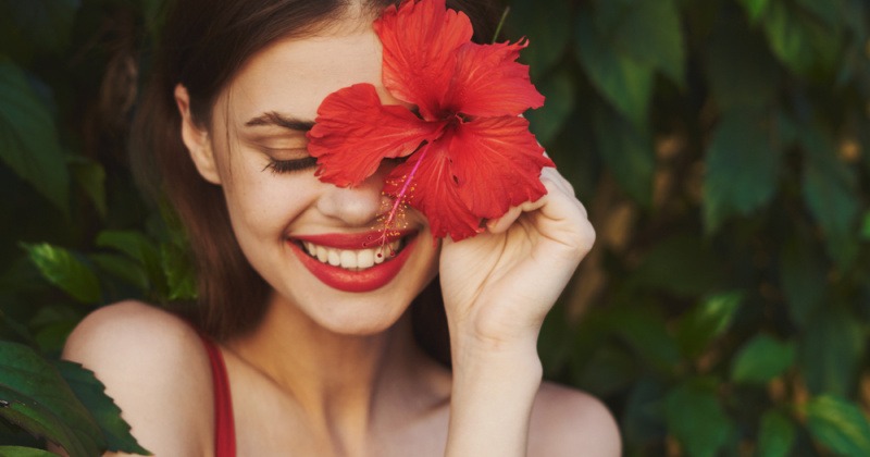 Eine Frau hält eine rote Blüte vor ihr Gesicht
