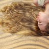Frau mit langen Haaren liegt im Sand und lässt die Haare von der Sonne aufhellen