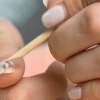 Frau benutzt Nagelholz, um Acrylnägel ohne Aceton zu entfernen