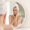 Frau steht nach Feuchtigkeitspflege für die Haut lächelnd vor dem Spiegel