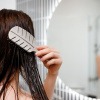 Eine Frau steht vor dem Spiegel und bürstet ihre nassen Haare