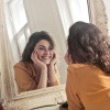 Frau betrachtet glücklich ihr Gesicht ohne Falten im Spiegel 