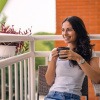 Lächelnde Frau sitzt am Balkon mit einer Tasse Tee