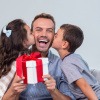 Tochter und Sohn küssen den Vater auf die Wangen, er hält ein Geschenk