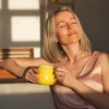 Frau mittleren Alters wird von der Sonne angestrahlt und wirkt zufrieden