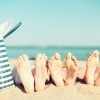 Füße liegen am Strand neben einer Badetasche