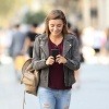 Eine junge Frau läuft in der Gegend herum und schaut dabei lächelnd auf ihr Smartphone.