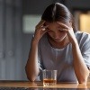 Eine junge Frau sitzt mit gesenktem Kopf vor einem alkoholischen Getränk