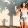 Eine fröhliche Frau reckt sich der Sonne entgegen, ihr Schatten ist in der Form eines jungen Mädchens mit Pferdeschwänzen.