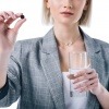 Frau mit einer Tablette Aktivkohle und einem Wasserglas