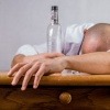 Ein Alkoholiker liegt am Tisch mit einer Flasche in der Hand