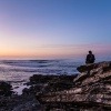 Ein Mann sitzt einsam und alleine auf Felsen am Meer